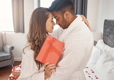 Buy stock photo Interracial couple, love bond or hug on valentines day date or anniversary celebration in house bedroom, hotel or home interior. Romantic trust, security or safety for indian man and woman with gift