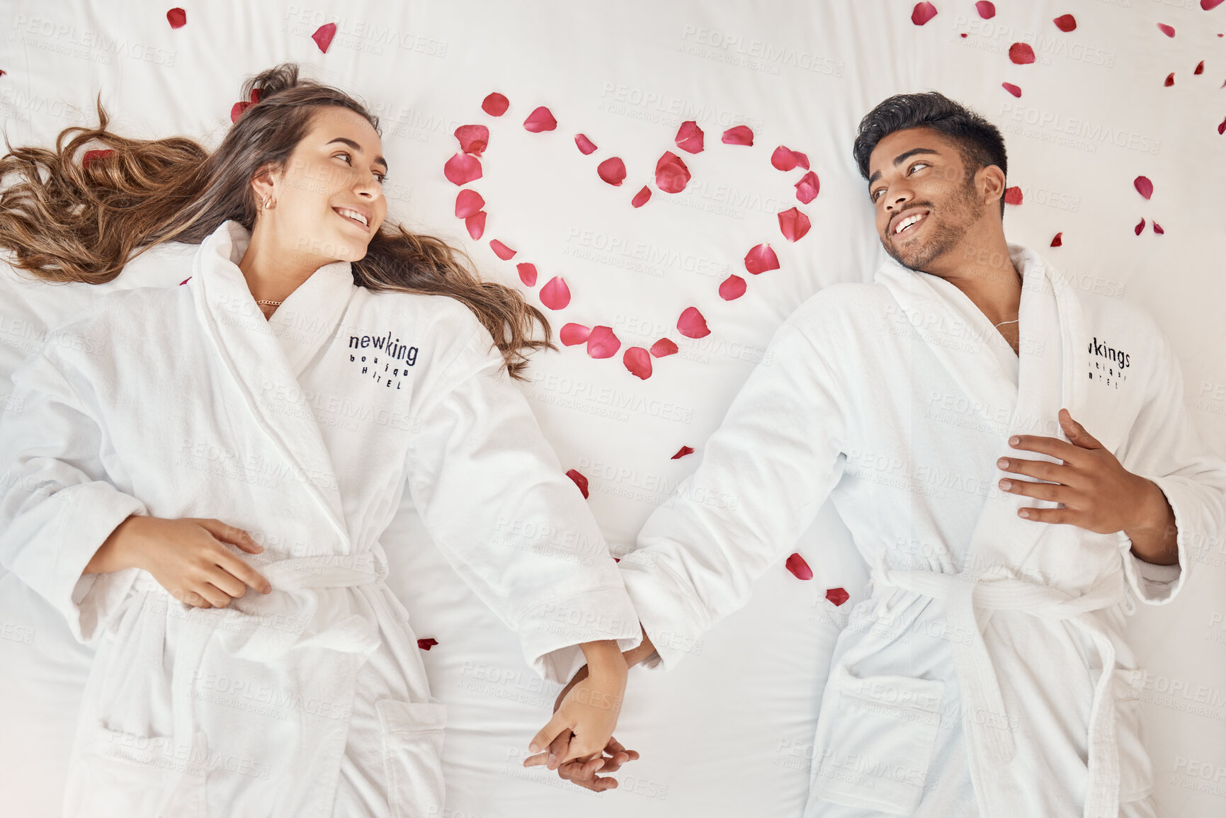 Buy stock photo Man and woman married couple on luxury bed celebrate honeymoon, love and relax in romantic vacation spa hotel. Happy, marriage and young people smile on valentines day with rose heart in bedroom