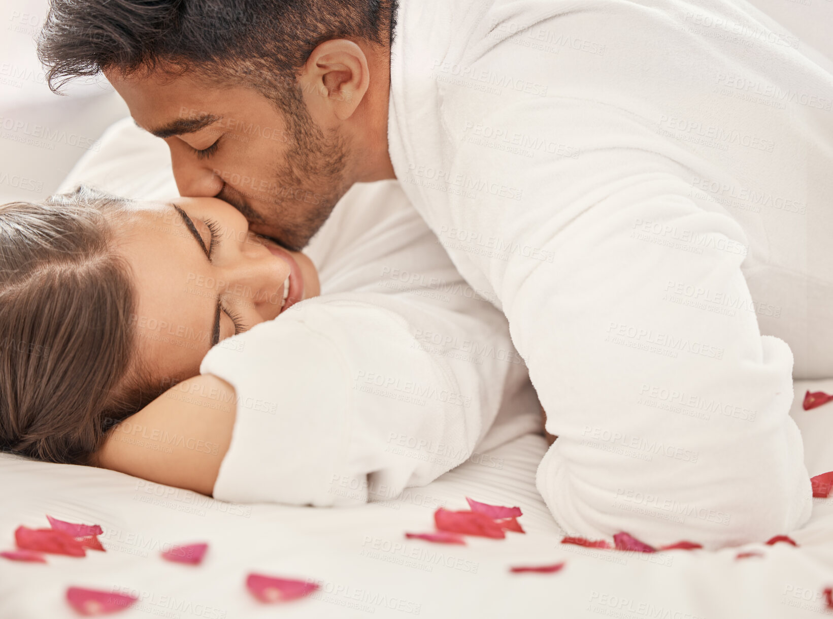 Buy stock photo Love, a kiss and rose petals, a couple in bed, happy and celebrating an engagement or honeymoon. Floral romance, marriage and a anniversary celebration of man and woman together on romantic holiday.