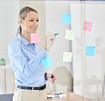 Writing, planning and thinking with sticky notes on a glass in a modern office. Happy woman manager, leader or ceo plan strategy on post it paper in a corporate marketing and advertising company