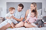 Family, morning love and happiness with caring parents sitting on the bed with their kids at home. Bond, playful and bedroom fun with a man and woman spending free time with  toddler children