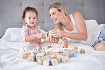 Happy mom on bed with young child, play game with toys for education or fun together. Mother smile in bedroom with toddler girl, learning alphabet and cognitive development in home with blocks