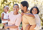Black family, nature and parents carrying children, bonding and spending free time on a sunny day. Support, love and happy caring man and woman on a walk at a park with their cute girls outside.

