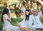 Friends, camera and photo on a picnic in a forest with food and drinks on green grass. Diversity, fun and happy women enjoy bonding together in nature with snacks while posing for a photo or picture