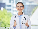 Portrait of a woman doctor showing thumbs up while standing in her office at the hospital. Happy, smile and professional healthcare worker doing a agreement gesture for a medical diagnosis in clinic.