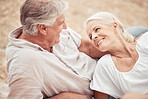 Senior couple, beach and vacation with a smile, love and together while relax on the sand together in summer. Elderly man and woman enjoy romantic holiday, anniversary or date at the ocean in nature 