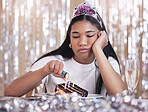 Sad, depression and angry woman at birthday celebration while lighting candle on cake. Lonely, depressed and frustrated female sitting at a party, fail and table  with snack, decoration and tiara 