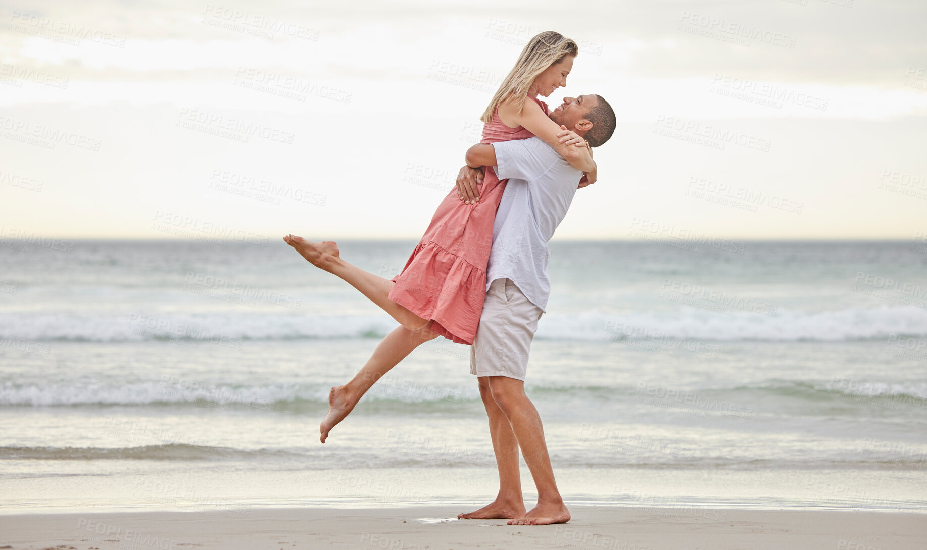 Buy stock photo Interracial couple, love and hugging on a beach by the water in holiday vacation in nature. Man and woman in joyful relationship affection together by the ocean in happiness for the outdoors