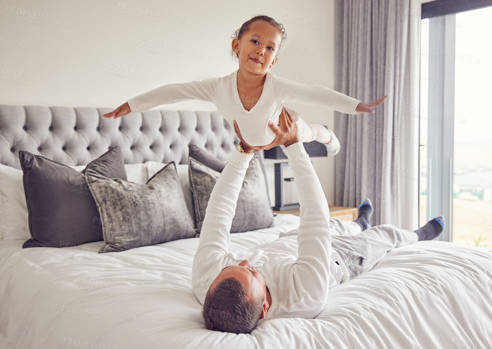 Buy stock photo Father lifting child in air on bed, playing and bonding in bedroom of house. Love portrait, care and trust of male parent holding happy kid up in house spending free time together having fun at home.