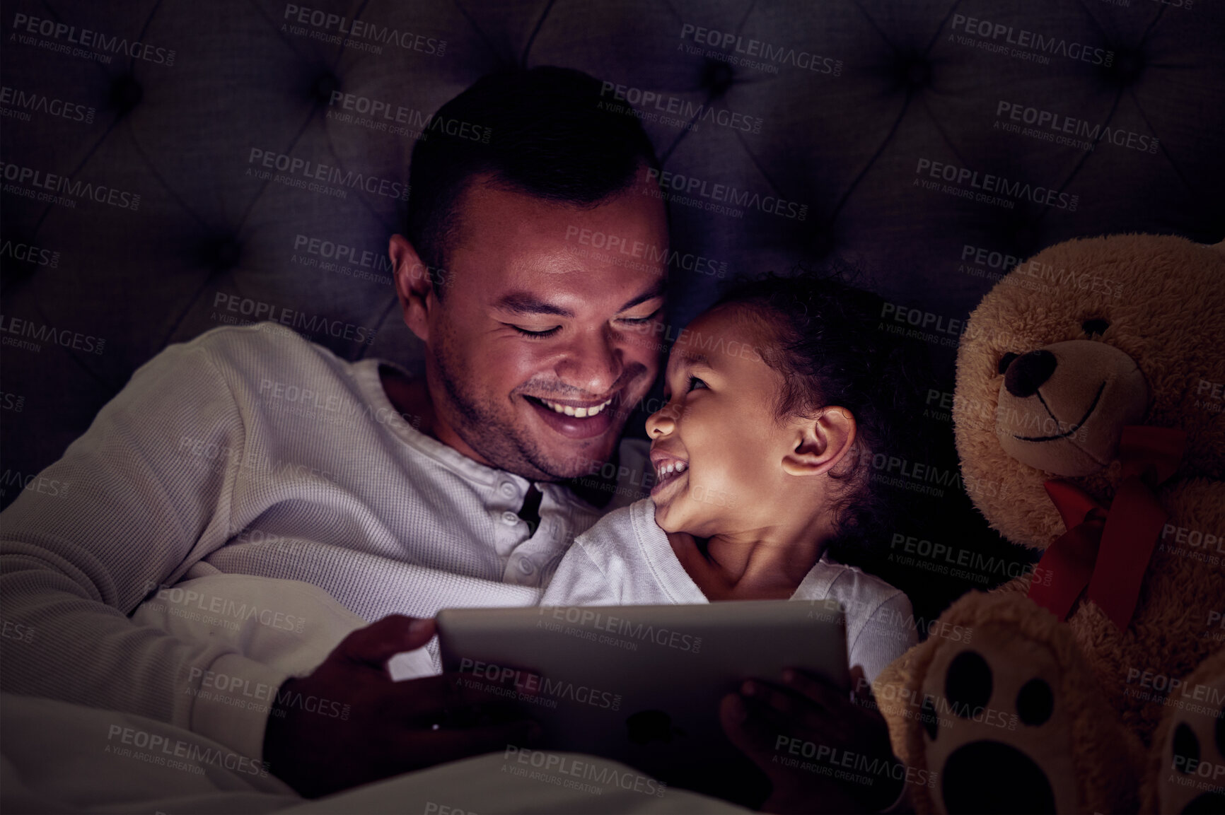Buy stock photo Father and child in bed with tablet reading ebook or to watch a film together at night. Happy girl with her dad enjoying online live streaming movie, game or digital kid app in dark home bedroom