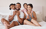 Young interracial couple smile on bed, with children in their home or apartment. Happy multicultural family, in bedroom with toddler kids while on weekend vacation or holiday together for portrait