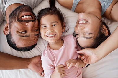 Buy stock photo Family, children and love with a girl and parents lying on the bed in a bedroom of their home together from above. Kids, happy and diversity with a mother, father and daughter bonding in their house