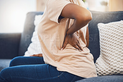 Buy stock photo Woman with a back injury, pain or accident from stress sitting on sofa in her living room. Black girl with a muscle sprain, back pain or injured spine medical emergency on couch in lounge at home.