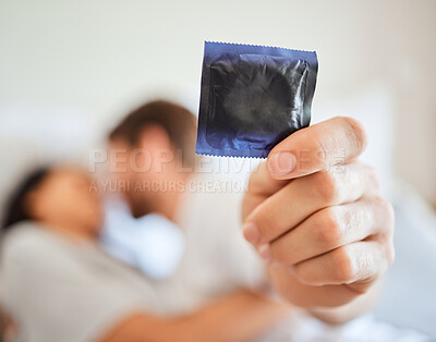 Buy stock photo Condom, safety and safe sex with couple in bed, foreplay and intimate bonding in their home together. Passionate man showing protection in hand while kissing and being sexual with a woman in bedroom
