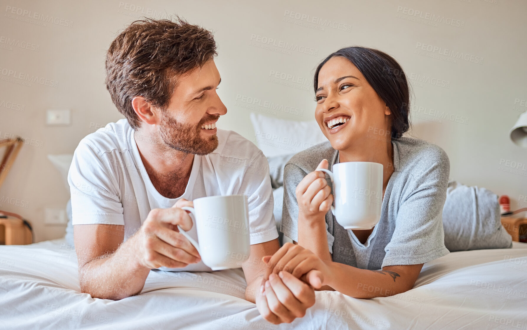 Buy stock photo Couple coffee, interracial smile and relax on bed in house, smile for love marriage and funny communication in bedroom of home. Man and woman happy with tea drink and comic conversation in morning