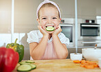 Cute girl with a smile eating cucumber, cooks healthy green salad for a meal and learning about nutrition benefits. Fresh fruit, organic vegetables and natural food is important for child development