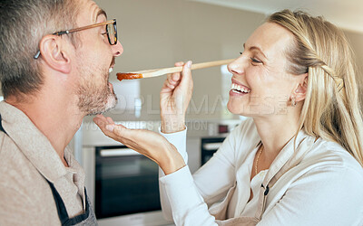 Buy stock photo Cooking woman feed man to taste food, meal and lunch in kitchen at home. Happy, smile and care wife giving, hungry and tasting husband mouth spoon of tomato sauce while couple eating dinner with love