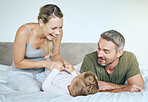 Happy family play and laugh together on the bed having fun at home on a weekend. Playful, love and carefree parents, mother and father bonding with their daughter, child or kid in the bedroom
