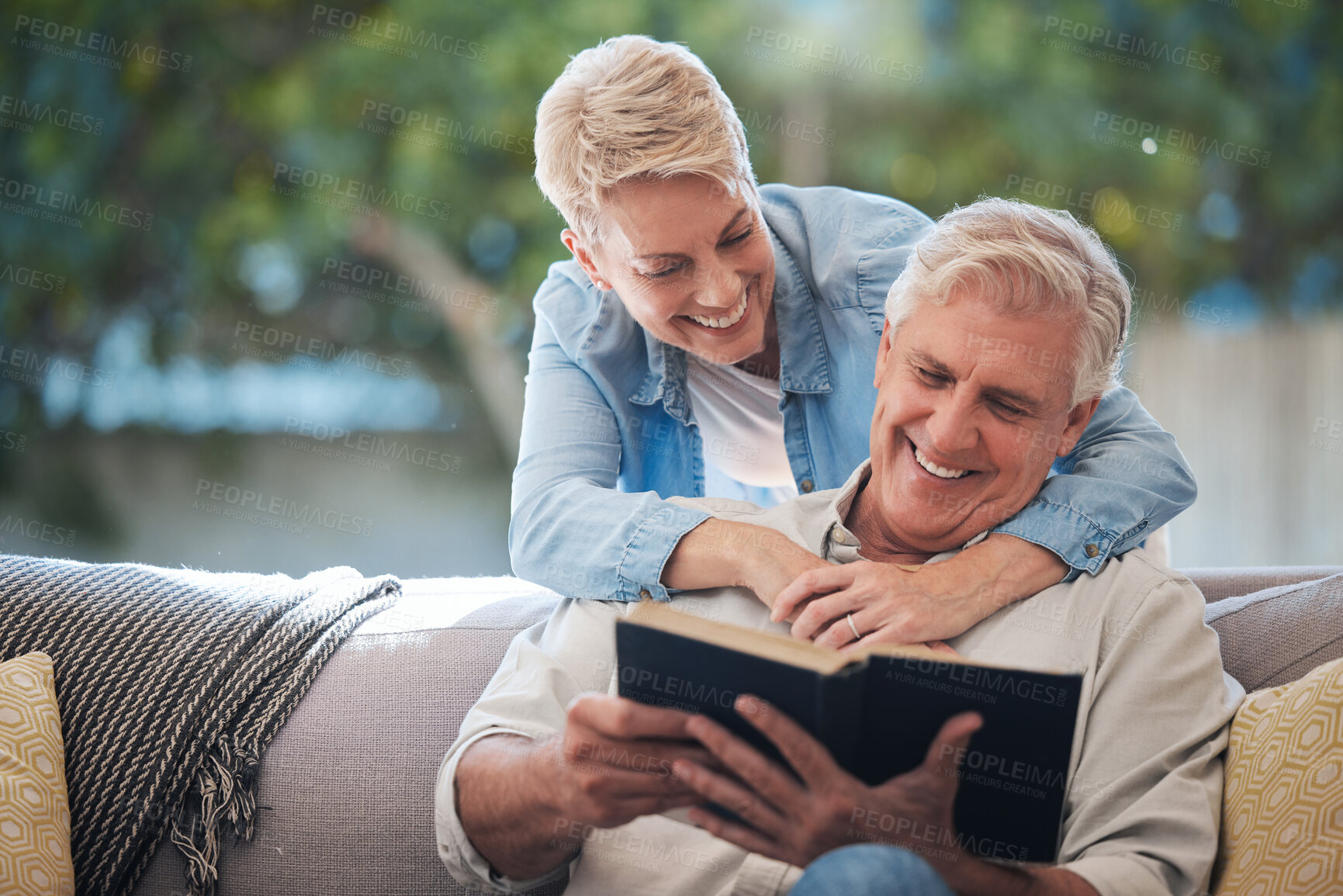 Buy stock photo Mature couple, bond and funny book on house or home sofa in garden and backyard patio. Smile, happy or relax senior man and elderly woman in retirement hug, trust or security love marriage with novel