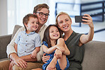 Family, happy and phone selfie on the sofa and smile for a social media post. Mother, father and kids together, bonding and carefree weekend in the living room and taking a picture with smartphone