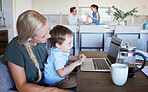 Mother, kid and laptop at table in living room with father and girl in background. Work from home mom on coffee break with son. Child development, family time and relax, a mothers love for children