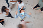 An angry woman with mask for covid and people walking around her. Young girl wearing face mask in a crowd, frustrated, mad and shaking her fist. Aerial view of upset female in a shop or mall