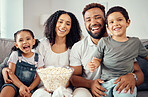  Love, laugh and having fun with a happy family eating popcorn, watching a movie and bonding together at home. Portrait of latino parents and children smile, enjoy the weekend and feeling carefree
