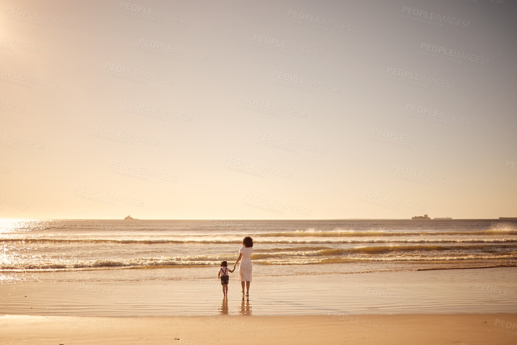 Buy stock photo Girl and mother walking in the water at the beach during sunset on summer family vacation. Young daughter and her mom on sand together by the ocean during the dusk on travel holiday with mockup space