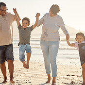 Happy kids playing with their excited grandparents at the beach on a ...