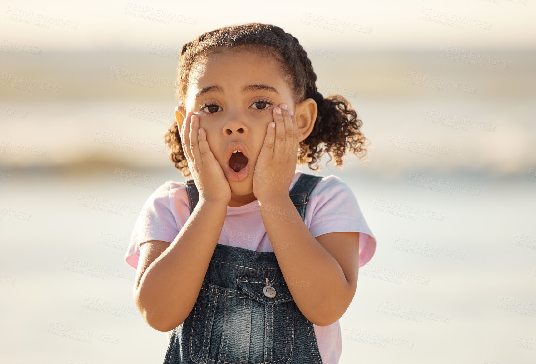 Buy stock photo Wow, children and hands on the face of a girl on the beach looking surprised or shocked outside during summer. Kids, youth and surprise with a little female child feeling shock while outdoor alone