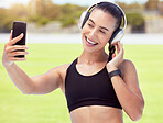 Phone, woman and fitness influencer taking a selfie at training, running and workout outdoors on sports racetrack. Smile, healthy and happy girl in headphones sharing fitness journey on social media