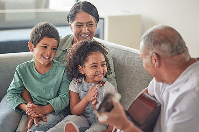 Buy stock photo Grandfather playing the guitar for grandmother and children sitting on the sofa in their home. Retired grandparents entertain happy and smiling grandchildren with music on acoustic guitar and bonding