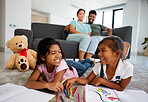 Happy little children drawing with parents in the background at home living room. Kids enjoying quality time and creative art together while man and woman babysitting children in the living room