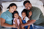 A happy black family in bed, mom and dad hold children with love. In their bedroom at home, little kids laugh as parents hug them with a smile on their faces and enjoy the quality time home together 