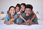 Portrait of a happy Asian family on the bed with a smile on their face. Multicultural Indian family in their bedroom smiling, laughing and having fun. Loving mom, dad and kids bond together at home