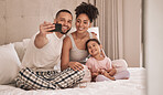 Selfie, phone and child with a mother, father and their girl kid sitting on a bed in their home. Daughter, family and parents with a man taking a picture while relaxing in a bedroom of the house