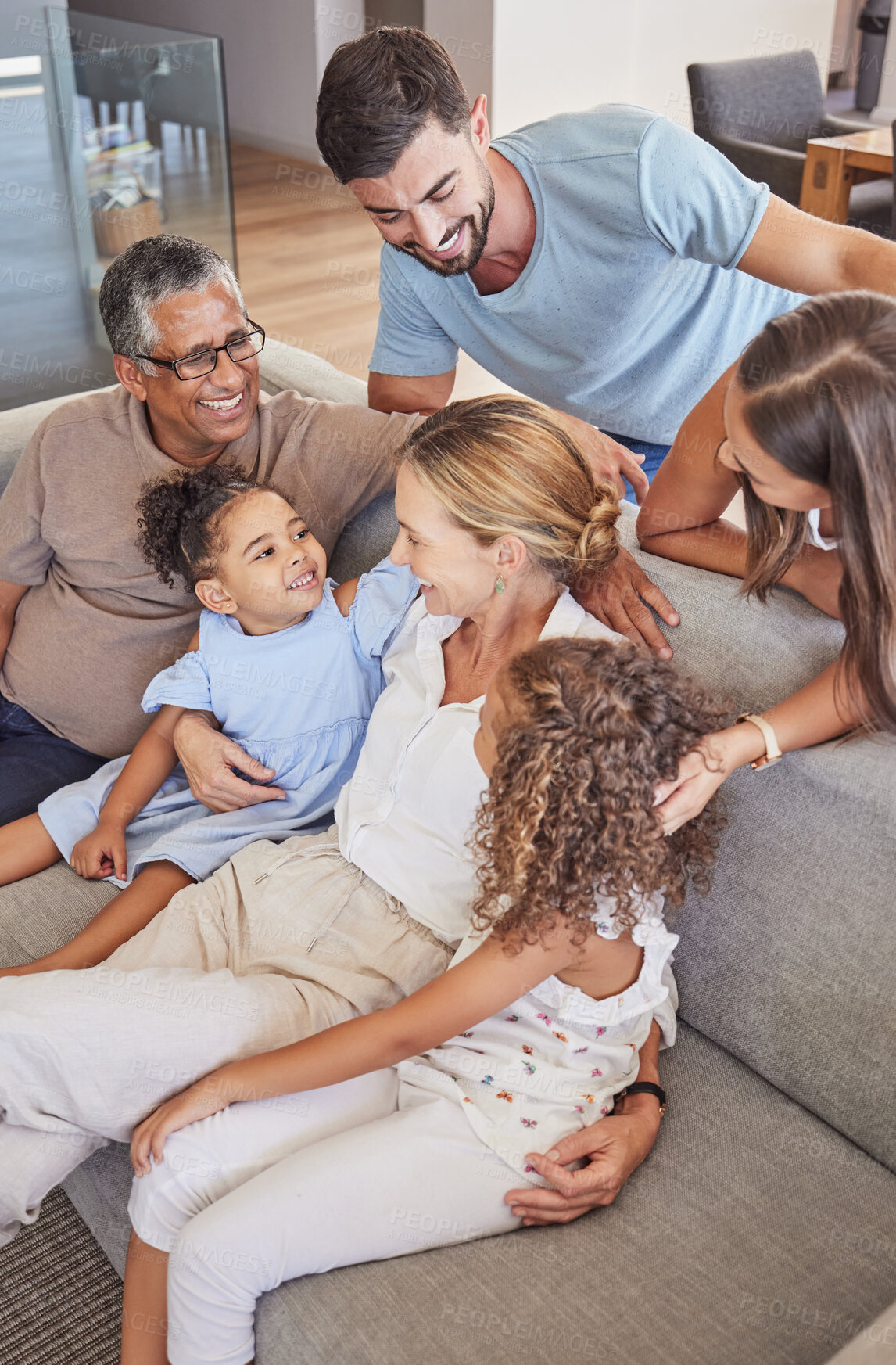Buy stock photo Happy interracial family bonding with their children and grandparents at home. Adults and their kids smile while sitting on the sofa, laugh and hug in a living room during vacation in a holiday house
