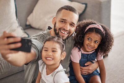 Buy stock photo Father taking a selfie on his phone with his children hugging and bonding in their family home. Multicultural father and daughters smiling, happy and taking a picture on their smartphone together
