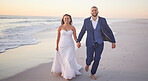 Wedding, couple and beach with a man and woman holding hands while walking on the sand by the ocean or sea. Love, trust and marriage with a bride and groom on the coast at sunset for celebration