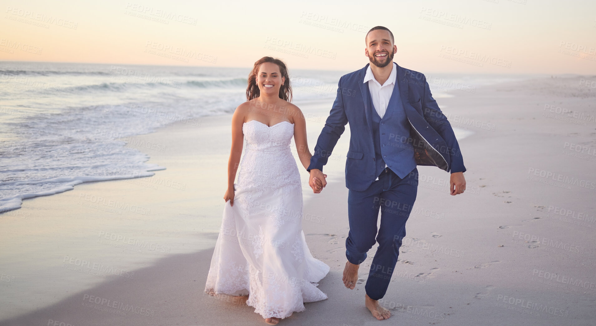 Buy stock photo Wedding, couple and beach with a man and woman holding hands while walking on the sand by the ocean or sea. Love, trust and marriage with a bride and groom on the coast at sunset for celebration
