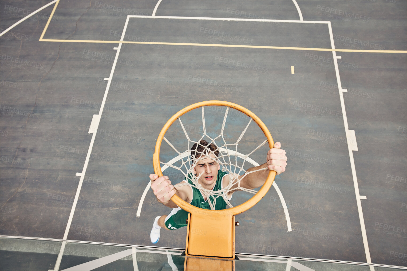 Buy stock photo Portrait of basketball player hanging on net on a basketball court. Young man playing basketball outside doing slam dunk and jumping to score a point. Motivation to win and have fun in sports game