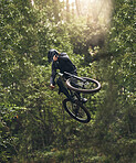 Cycling, bicycle jump and sports man travel in Japan nature forest for adventure, motivation and extreme sport journey. Trees, talent and bike rider or cyclist training in woods for exercise fitness