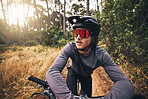 Cyclist, bike and forest on adventure in nature for health, fitness and wellness. Man, bicycle and sunglasses in woods for travel with helmet on training, exercise or workout on trail by trees