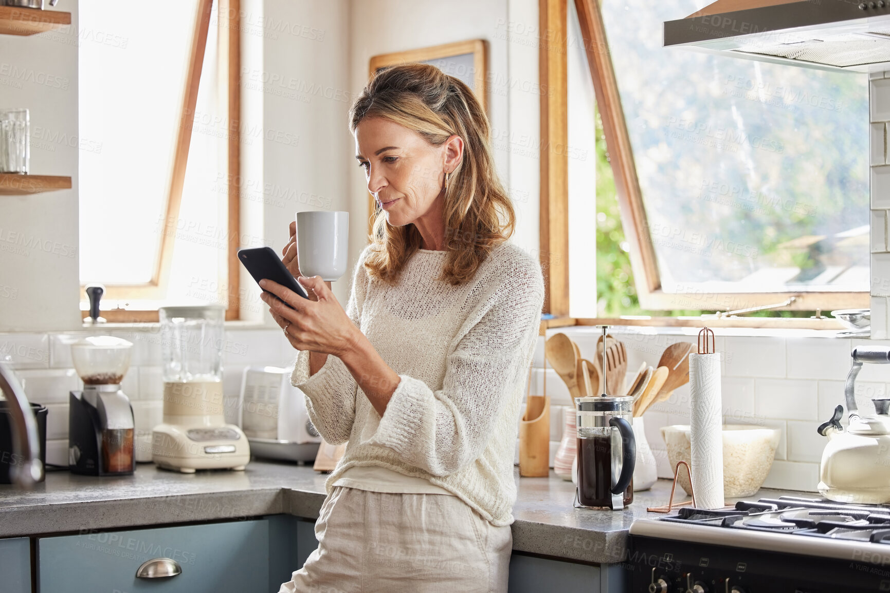 Buy stock photo Coffee, phone and senior woman in kitchen browsing social media, text message or online app at home. Relax, tea and reading news or mobile online web surfing with female from Canada on 5g smartphone
