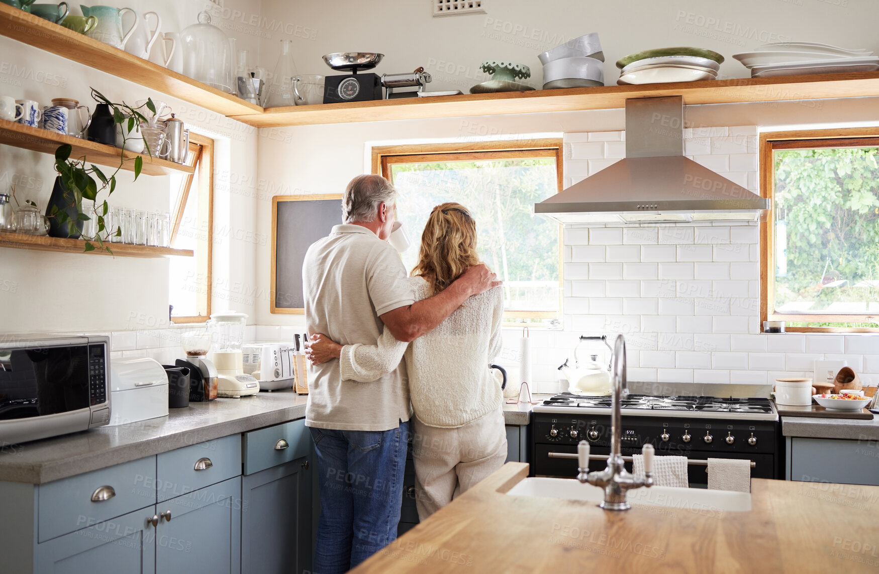 Buy stock photo Couple hug, morning coffee and senior people having breakfast in the kitchen while looking at outdoor nature. Elderly man and woman hugging with tea drink in house with love together from behind