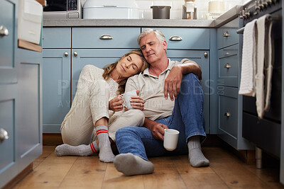 Buy stock photo Senior couple, love and support while sitting together feeling safe, relax and calm drinking coffee and bonding comfortable on a kitchen floor. Happy old man and woman enjoying retirement together