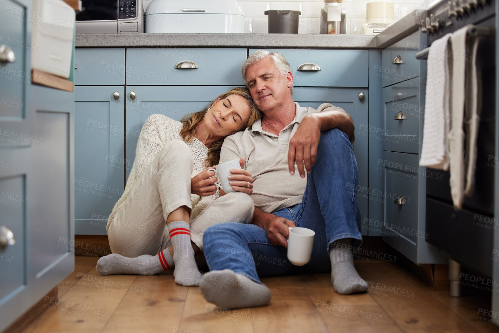 Buy stock photo Senior couple, love and support while sitting together feeling safe, relax and calm drinking coffee and bonding comfortable on a kitchen floor. Happy old man and woman enjoying retirement together