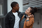 Young couple with headphones walking in the city on the street. Love, dating and woman holding hands with black man in multicultural relationship, smiling and hugging while taking walk in urban town