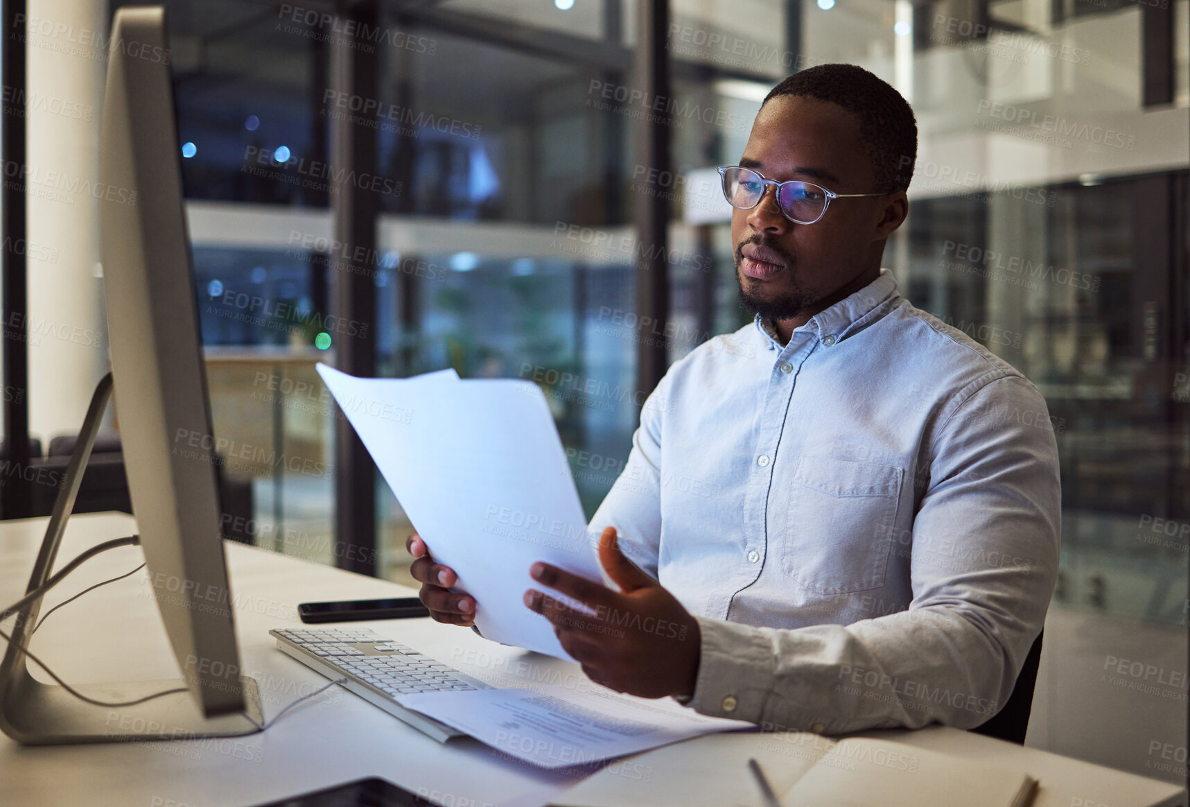 Buy stock photo Night worker, black businessman and paperwork planning, reading documents and financial reports at desktop computer in Jamaica. Young focus entrepreneur working expert strategy in dark modern office