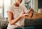 Diabetes, health and elderly woman doing a blood sugar test on her finger with a glucometer. Sickness, healthcare and diabetic senior lady checking her glucose level sitting on a sofa at home.